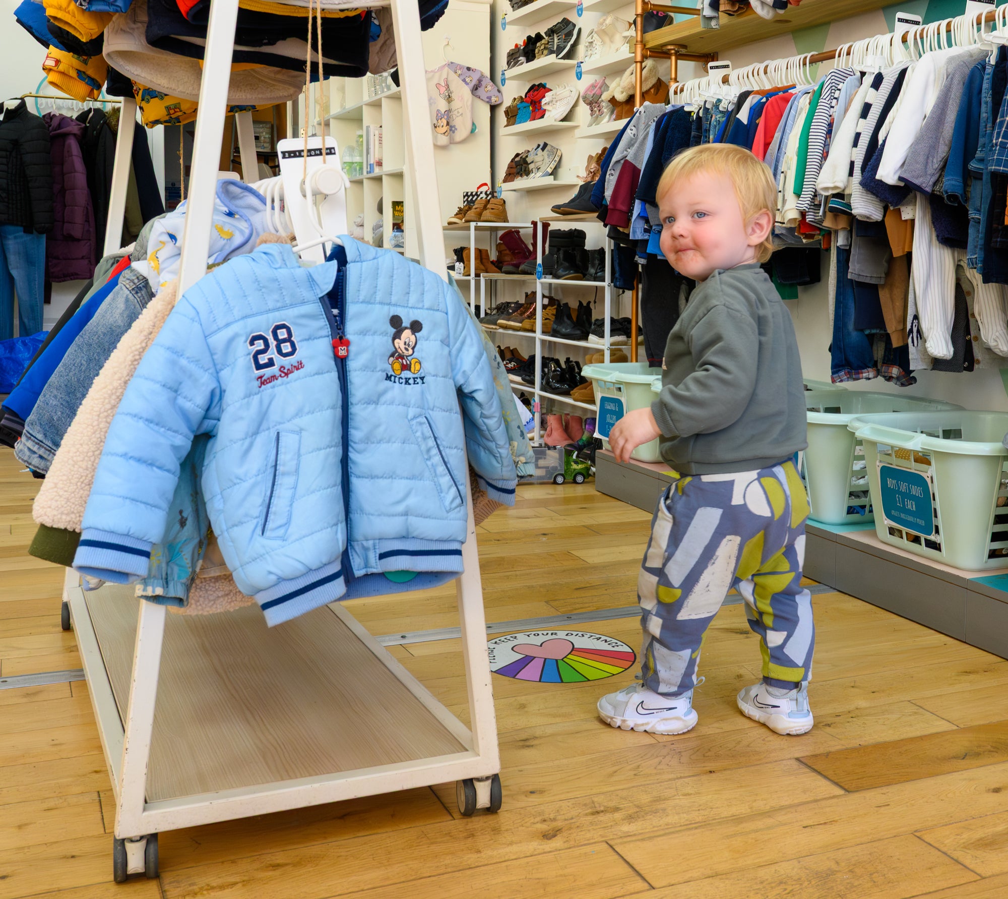 Child standing next to a clothing rack with jackets in a store